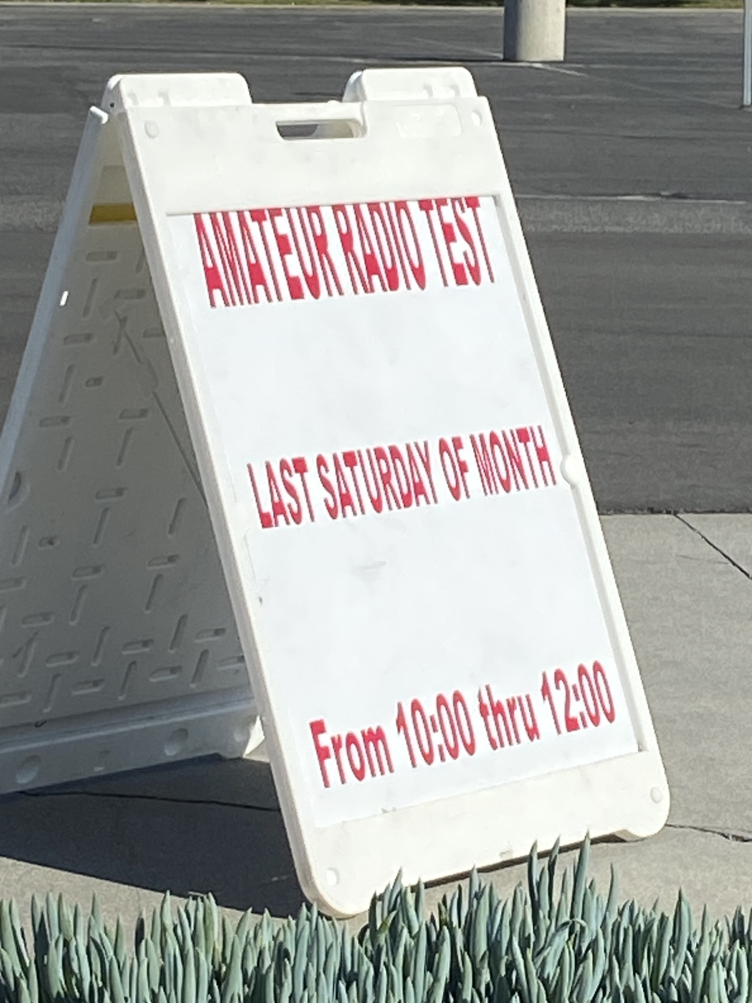 A white plastic freestanding sign that says “amateur radio test last Saturday of month from 10 AM through noon