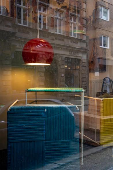 Rote Lampe mit farbigen Stühlen in der Auslage eines Schaufensters hinter Reflexionen.