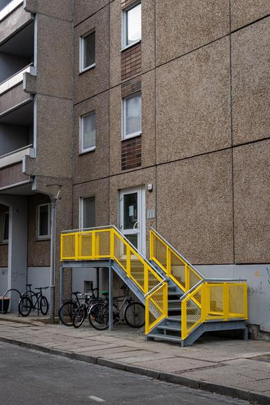 Gelbes Treppengeländer an einem Aufgang eines Plattenbaus in einer farblosen Szene.