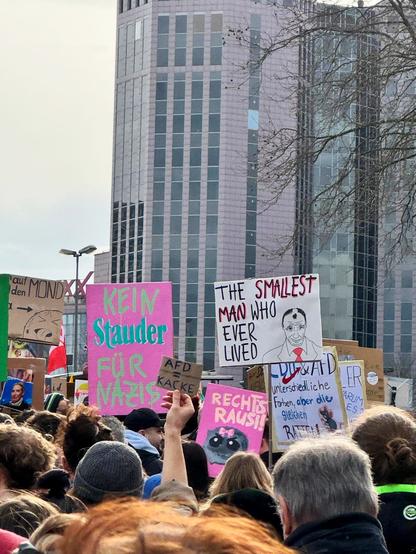 Bild einer Demo, viele Demonstrant:innen und Demo-Plakate, darunter: "Kein Stauder für Nazis", "The smallest man who ever lived" mit einer Karikatur von Friedrich Merz, "Rechtis Rausi" mit einem Bild von einem böse dreinblickenden Hamsti und "AFD =Kacke"