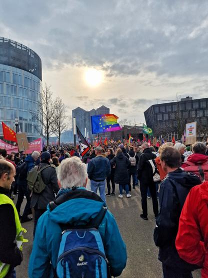 Bild einer Demo, viele Demonstrant:innen, in der Mitte weht eine Flagge, halb Europaflagge, halb Regenbogenflagge. Im Hintergrund sind die Weststadttürme in Essen zu sehen.