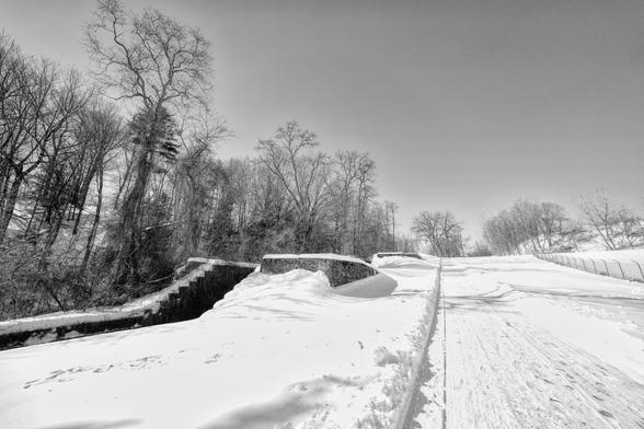 A black and white winter image of a trail alongside an old, stepped, granite canal structure.