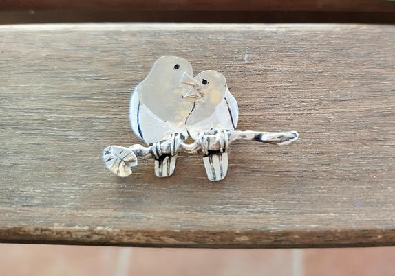a silver pendant. it's two loving birds on a branch.