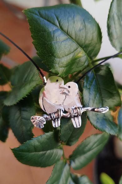 a silver pendant. it's two loving birds on a branch. it's placed on green leaves