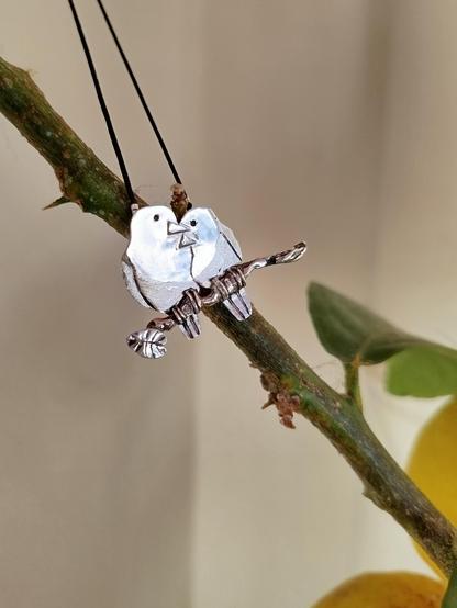 a silver pendant. it's two loving birds on a branch. it's placed on real branch