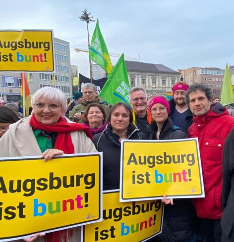 Eine Gruppe Menschen mit Schildern "Augsburg ist bunt" in ihren Händen. Von links nach rechts: Claudia Roth, für die Grünen in Augsburg im Bundestag und Kultur-Staatsministerin, Christine Kamm, Martina Wild, Augsburgs zweite Bürgermeisterin, Jürgen Enninger, Kulturreferent der Stadt Augsburg, ich, Marie Rechthaler, Markus Schnitzler, Sprecher der Grünen in Augsburg, und Deniz Anan.