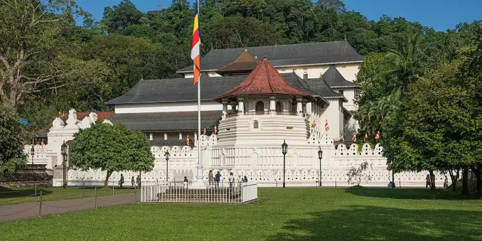 The image depicts a historical building surrounded by greenery. The architecture features distinct elements such as a white facade, a terracotta roof, and ornate designs. Additionally, there are flags, possibly representing different communities or nations, and it seems to be set in a park-like environment, suggesting a place of significance, likely a cultural or religious site.

Image Credits: Wikimedia / A.Savin / FAL