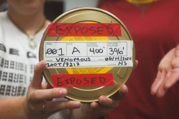 A closed 16mm film canister - held to the lens by the cinematographer - reads “Exposed. Roll 001. MAG A. Loaded film 400ft. Exposed film 396ft. Production - Venomous by Shae Altered
