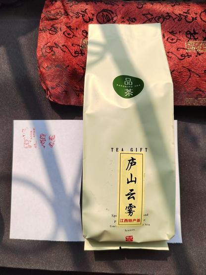 A closer-up view of the sealed bag holding the tea.  It's a plain bag, not branded, that has some generic "this is tea"-style marking over which is slapped a vertical sticker reading "Lushan Cloud and Mist" (in Chinese, naturally) from top down in black, then across the bottom in small red type "Jiangxi Speciality Tea".  The seal stamps are still a little blurry here so will be described later in a picture that has them in better focus.