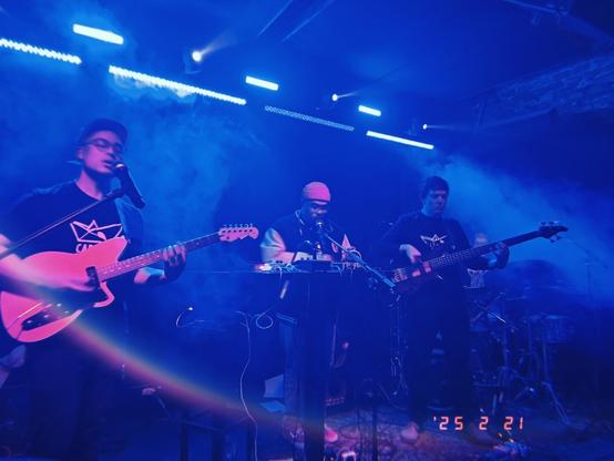 A baoyband with instruments in stage perfoming. Blue lights are dominating.