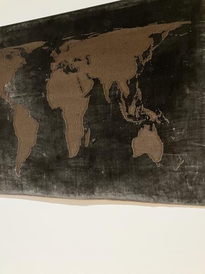 Black velvet and brown corduroy textured tapestry depicting a map of the world with the velvet creating the water.