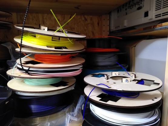 A shelf full of filament for 3d printing, some of it on the mentioned wooden spools.