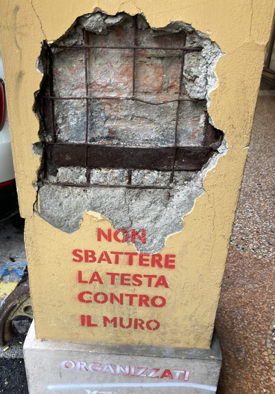 La foto mostra una grande crepa in un muro con la scritta:” Non sbattere la testa contro il muro, organizzati”