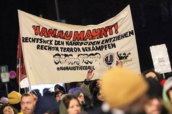 Das Foto zeigt ein Transparent mit dem Text: "Hanau mahnt! Rechtsruck den Boden entziehen - rechten Terror bekämpfen" sowie Portraits von Gökhan Gültekin, Sedat Gürbüz, Said Nesar Hashemi, Mercedes Kierpacz, Hamza Kurtović, Vili Viorel Păun, Fatih Saraçoğlu, Kaloyan Velkov und Ferhat Unvar und dem Hastag #HanauIstÜberall