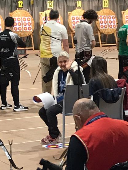 La nostra Giovanna, volontaria ai campionati, seduta. Sullo sfondo arcieri sulla linea di tiro