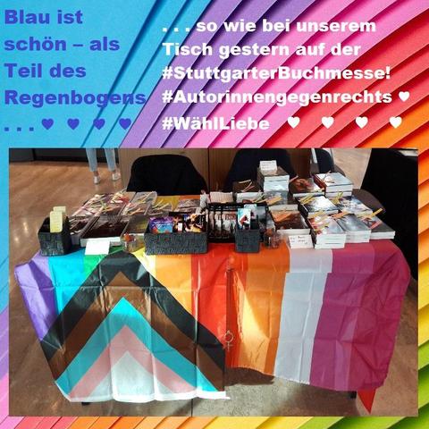 Ein Regenbogenhintergrund mit einem Foto von einem Buchmessentisch mit Büchern und Werbematerial sowie einer Regenbogenflagge und Lesbenflagge, darüber der obenstehende Text.