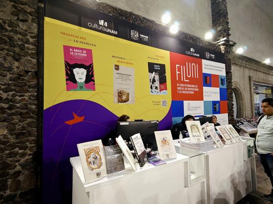 En el stand de Libros UNAM dentro de la Feria Internacional del Libro del Palacio de Minería, un panel anuncia de manera destacada la antología "El Ángel de lo Extraño"