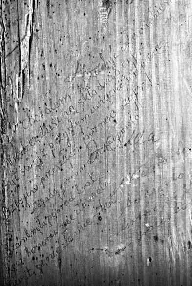 Black and white image of an aged wooden surface with faded handwritten text, possibly historical, inscribed across it.
