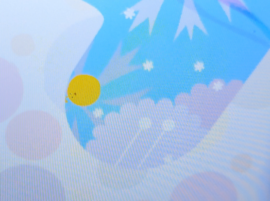 Screenshot of the game LocoRoco on PSP. It features a happy yellow blob, constantly rolling and jumping through a colorful world filled with bird noises, an uplifting soundtrack and happy flowers and beasts all around.