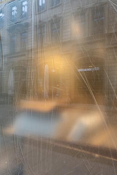 Blick auf eine mit Folie verdeckte Schaufensterscheibe, in der sie das gegenüberliegende Haus spiegelt.