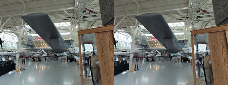 Stereoscopic, parallel view. Interior of an air museum, looking along the right wing of a very large seaplane which absolutely dwarfs the other exhibits. It has a boat-like body, pontoons coming from below the wing tips, and is painted military grey.