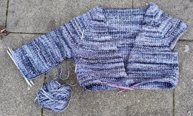 A cardigan knitting project in progress. 

The body is about waist length, one sleeve about 2/3 done. Yarn is stripey and in shades of blue and grey, it's worked in a textured pattern stitch.