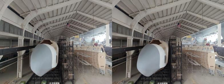 Stereoscopic, parallel view. A diorama of the construction of the Spruce Goose seaplane. We are inside a recreation of the hanger in which it was built, looking from the front of the plane along the left side. On the right of the image, we can see the ribs of a wing being built.