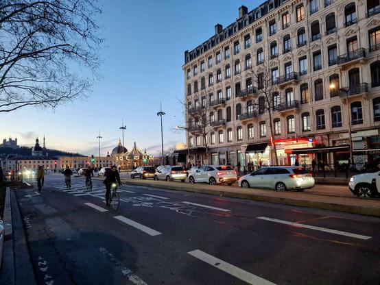 le cours Gambetta avec un immeuble de style haussmannien/vaïsse et en fond le grand hôtel dieu et la basilique notre dame de Fourvière.
au premier plan des cyclistes avancent vers moi