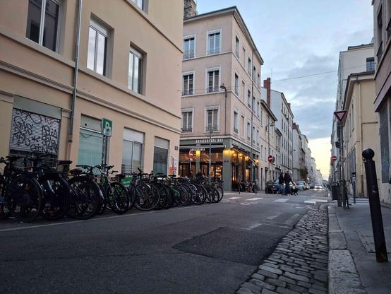 rue pasteur avec un parking vélo surchargé et juste après le bar Abracadabra illuminé