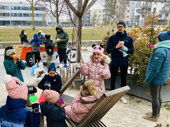 Eine Menschengruppe steht an der Seestadt Lounge und trinkt gemeinsam punsch. Im Hintergrund sieht man ein Lastenrad zum gießen der Pflanzen