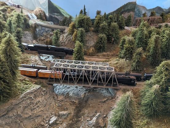3 trains pass one another across a bridge over a small creekbed