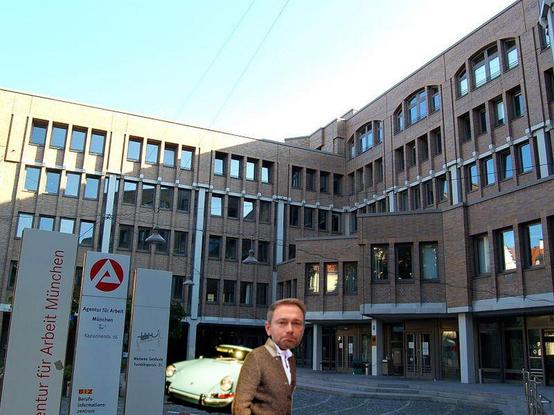 Christian Linder steht traurig vor einem Porsche vor der Agentur für Arbeit