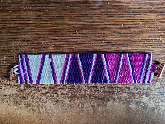 The bracelet flat out. The design is triplets of three triangles in same colors separated by diagonal lines. From L-R: matte white, silver-lined purple, silver-lined hot pink.