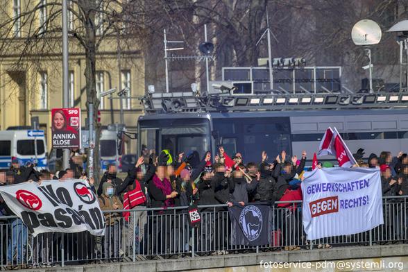 gegenprotest an einem geländer, im hintergrund der protestbus der gruppe "zentrum für politische schönheit", banner: "no pasaran" und "gewerkschaften gegen rechts!"