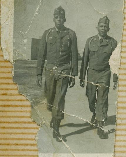Erma Hayman House flyer with partially torn old black and white photo of two Black soldiers walking down street set on sticky page of old family photo album with horizontal glue lines showing behind