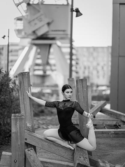 Black and white photography of a woman doing ballet poses on wooden planks in front of a crane in the docks of Hafen City Hamburg