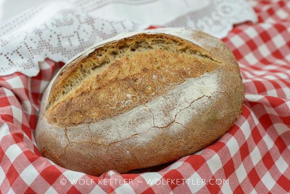 A loaf of crusty, rustic bread on a red and white checked piece of fabric.