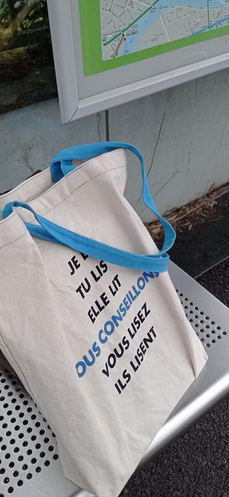 Tote bag de librairie. Il est écrit "je lis, tu lis, elle lit, nous conseillons, vous lisez, ils lisent"