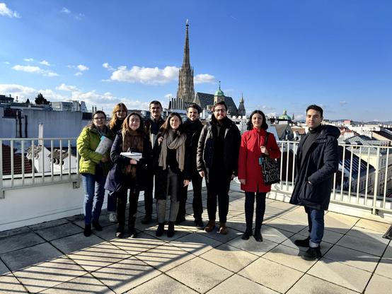 Gruppenfoto mit acht Volontär:innen und einer Wissenschaftlerin vom ACDH-CH auf der Terrasse der ÖAW in Wien. Im Hintergrund ist der Stephansdom zu erkennen. Es ist sonnig.