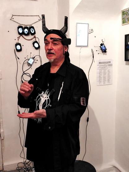 Yann Minh in front of the exhibit by Sigrid Coggins of videos presented on Grenade Vijou, jewels shaped like a WW1 hand grenade integrating an oval video screen, and Digital Bug, a video screen shaped like a crawling bug.