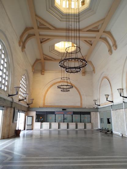 Inside the old Casa Voyageurs ticket hall. Marble floors, white arched walls and high vaulted ceilings with chandeliers. The closed ticket booths are at the back.