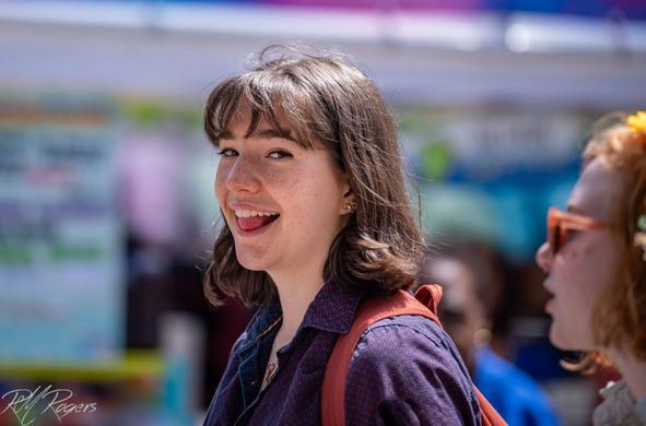 A young woman with freckles smiles when she catches the photographer taking her picture on the street.