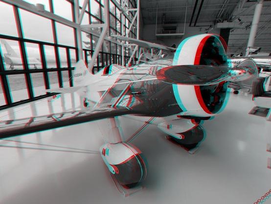 Inside an air museum, a beautiful, bulbous 1930s racing monoplane with a chrome propeller. Stereoscopic, black and white view for anaglyph (red/blue) glasses.