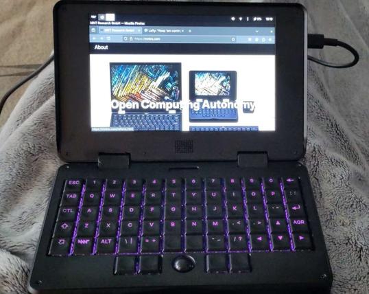 Ein aufgeklappter Mini-Laptop mit violett beleuchteten Tasten. Der Bildschirm zeigt die Webseite von MNT Research https://mntre.com