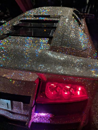 Rear 3 quarters perspective view of a Lamborghini murcielago completely covered in tiny white and pink crystals.