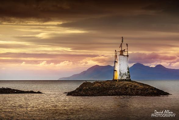 In the Western Scottish Highlands, the rocky islet of Sgeir Dhearg, with its lighthouse, in the Sound of Sleet. In the far distance, the romantic Isle of Skye.