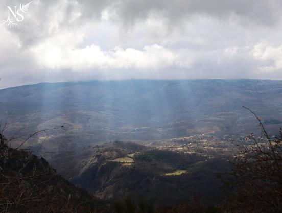 English A mountain landscape seen from a distance and altitude. There are sunrays passing through the clouds and shedding light on meadows and a village.
•
Français Un paysage de montagne vu de loin et en altitude. Des rayons de soleil percent les nuages pour éclairer des prairies et un village.