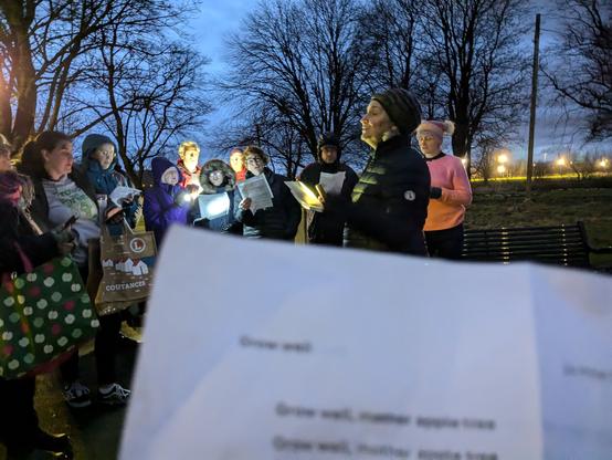 Group of singers at the Community Orchard singing to the apple trees