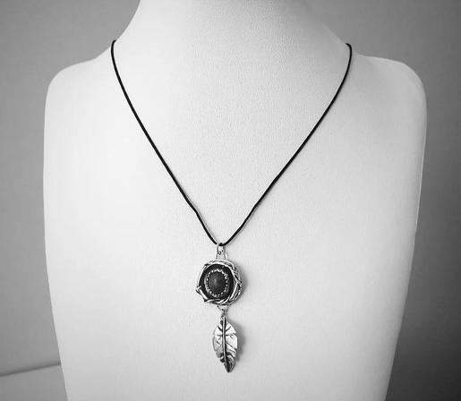 a pendant with a silver leaf and a circle above it. the photo is black and white