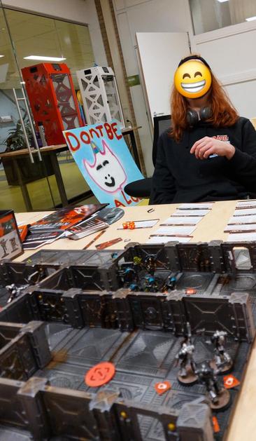 Student at the other side of the kill team board grinning and not scratching his thing because he did not get the chin itch bug. In the front there are some space marine types and tokens aplenty